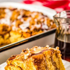 A slice of pumpkin French toast casserole on a white plate with syrup poured on top.