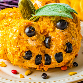 A pumpkin cheese ball with a jack o lantern face made with olives on a white plate.