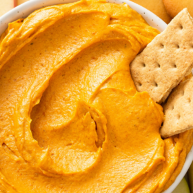 Up close image of pumpkin dip in a white bowl with two graham crackers dipped in it.