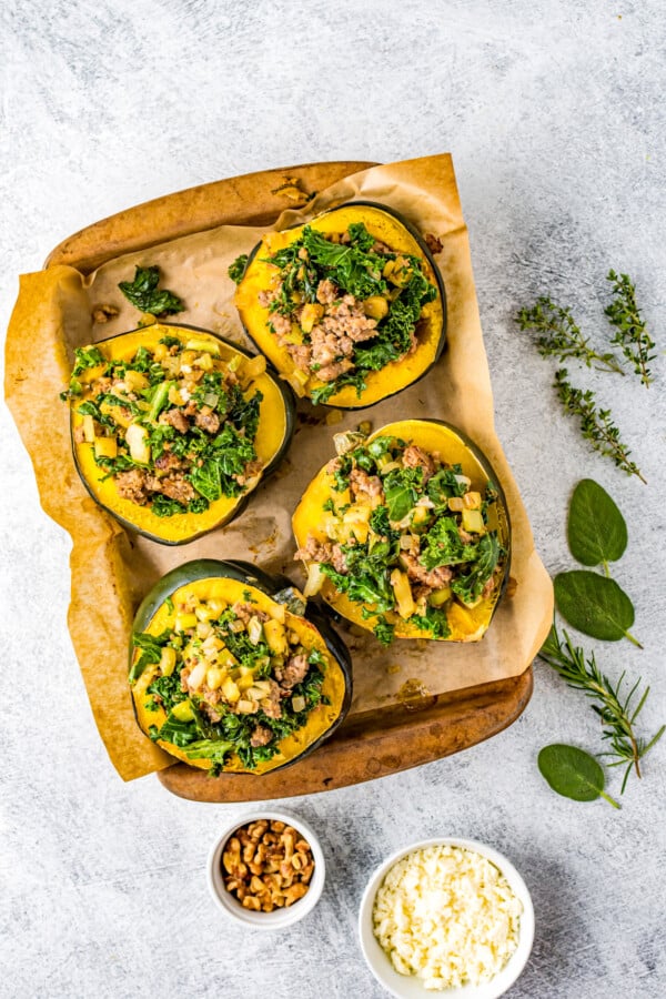 A wooden tray with four unbaked stuffed squash halves.