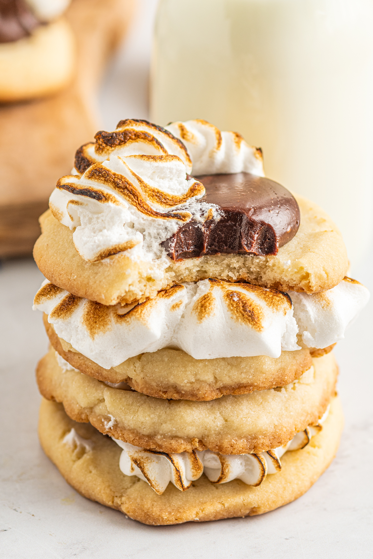 A close-up shot of four s'mores cookies, stacked on top of each other. The top cookie has had a bite taken out of it.