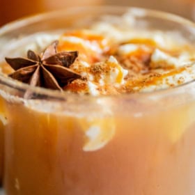 Up close image of a clear mug filled with apple cider with whip cream on top.