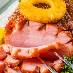 A cooked ham sliced on a platter with pineapple on top.