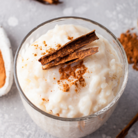 Arroz Con Leche in a glass jar with cinnamon on top and cinnamon sticks around the glass.