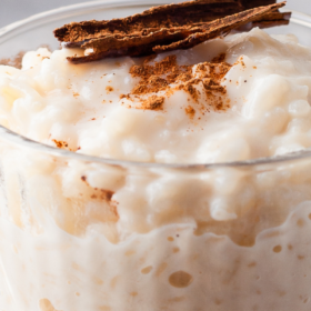 A bowl full of Arroz Con Leche in a glass jar with cinnamon on top.