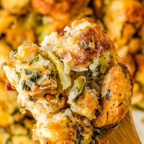 A spoonful of homemade stuffing being lifted from a casserole dish.