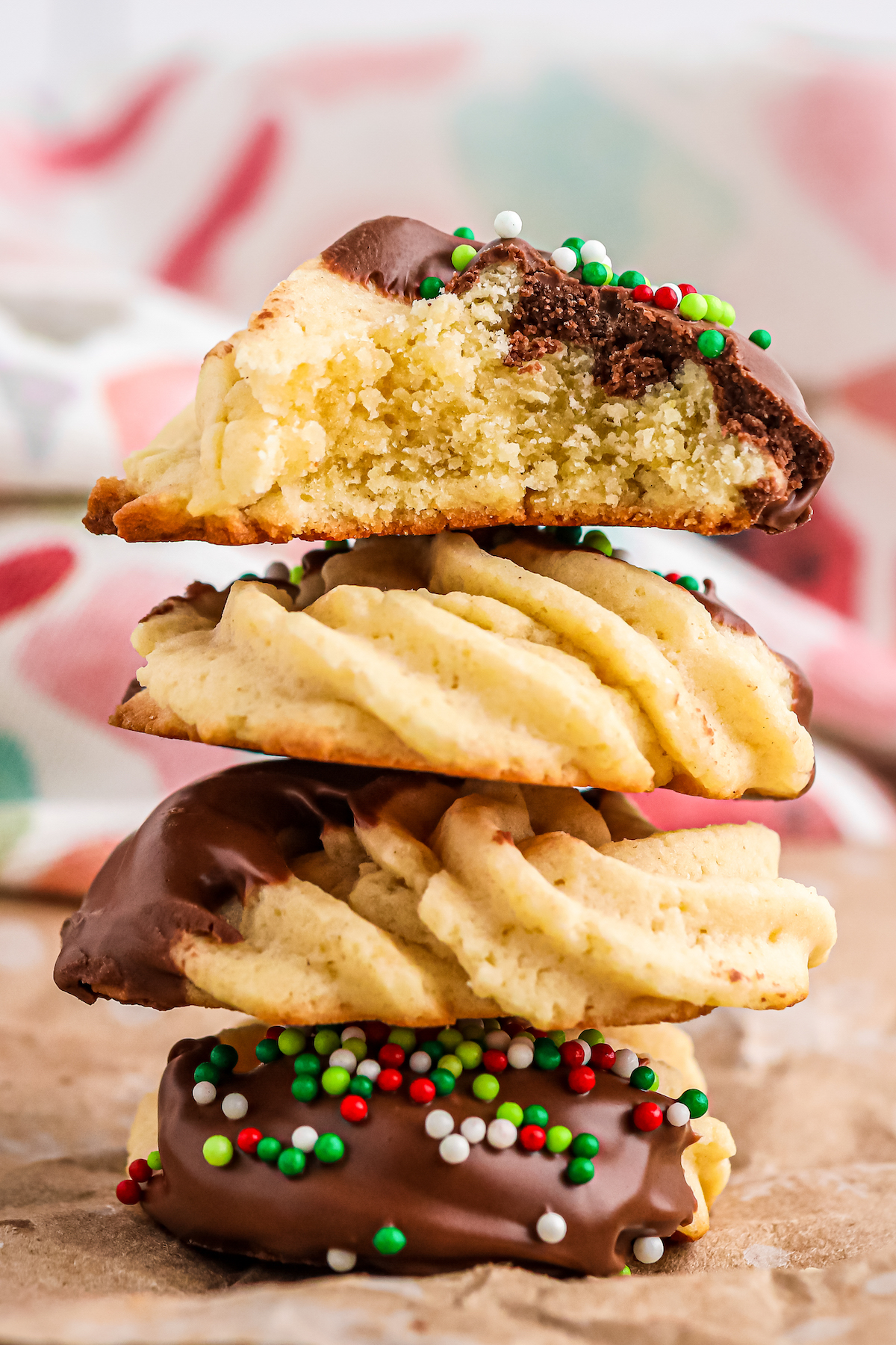 Four danish butter cookies stacked on top of each other. The top cookie has had a bite taken from it. Christmas wrapping paper is in the background.