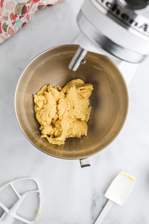 An overhead shot of the bowl of a stand mixer, with a soft ball of cookie dough inside.