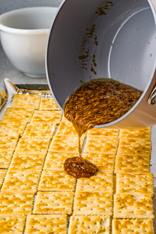 Hot butter toffee being poured out of a saucepan over a baking tray of saltine crackers.