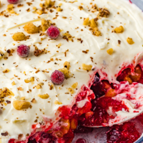 Cranberry jello salad in a glass bowl with cream cheese frosting on top with three big scoops removed to show the inside.