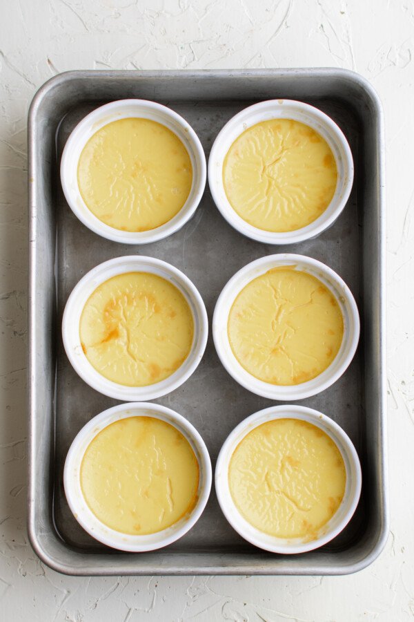 Six ramekins in a baking pan, with baked egg custard in each ramekin.