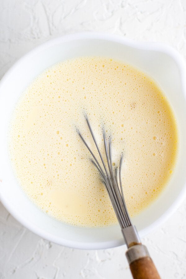 An uncooked custard mixture in a mixing bowl, with a whisk resting in the mixture.