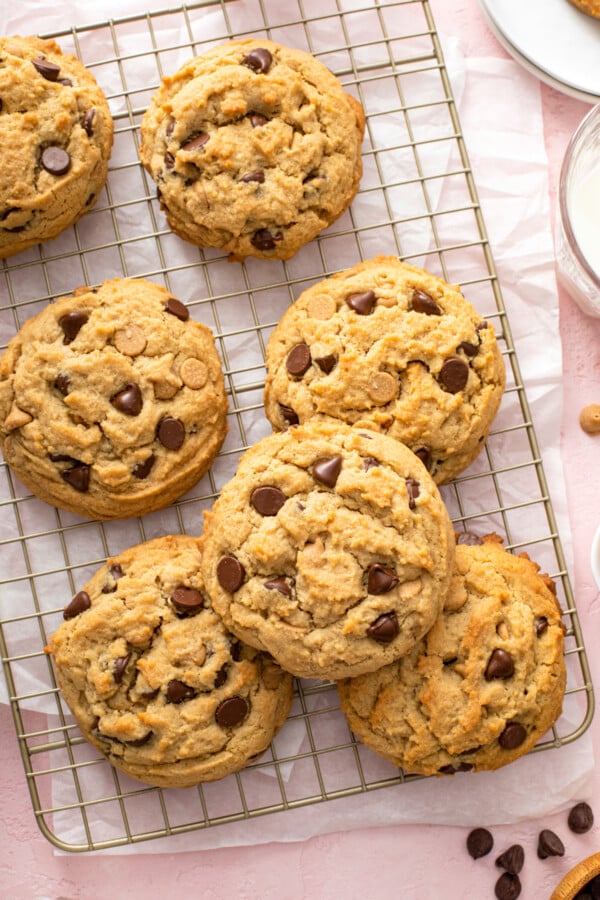 Seven large cookies on a cooling rack, with chocolate chips scattered on the work surface.