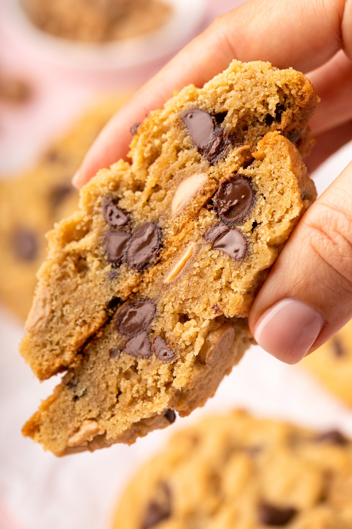 A hand holding two halves of a large cookie, cut halves facing the camera to show the cookie's texture.