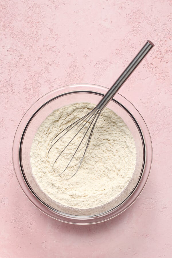 A mixing bowl with a whisk and white flour mixture inside.