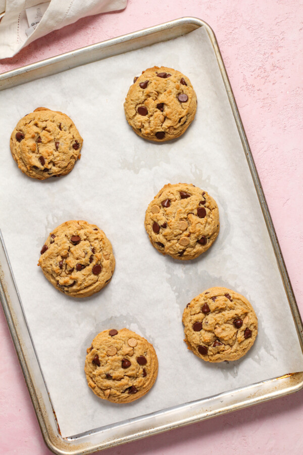 A parchment-lined baking sheet with six large cookies on it.