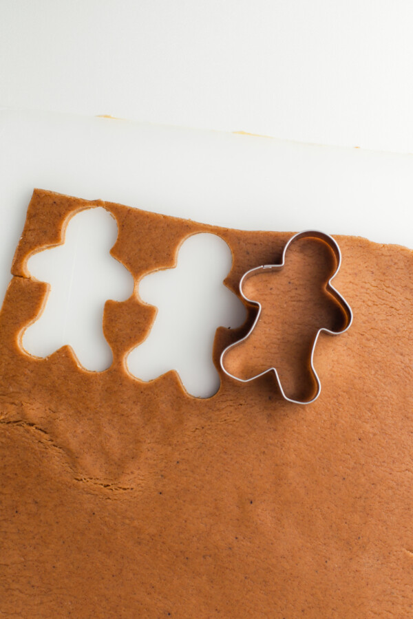 A sheet of cookie dough with two gingerbread men shapes cut out of it, and a cookie cutter resting on the dough.