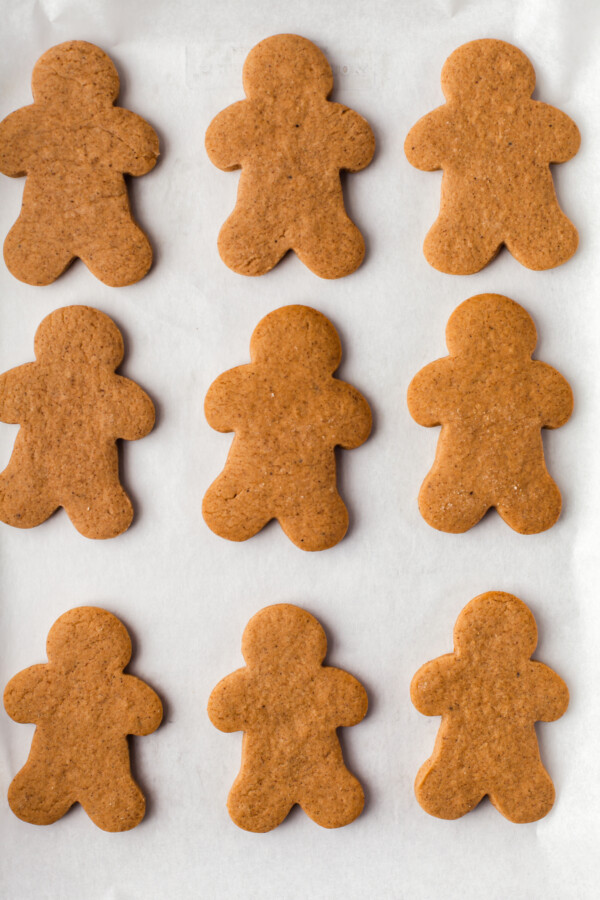 Rows of un-decorated gingerbread men on a parchment-lined surface.