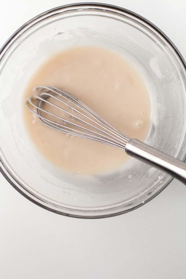 A bowl of creamy icing with a whisk resting in the mixture.