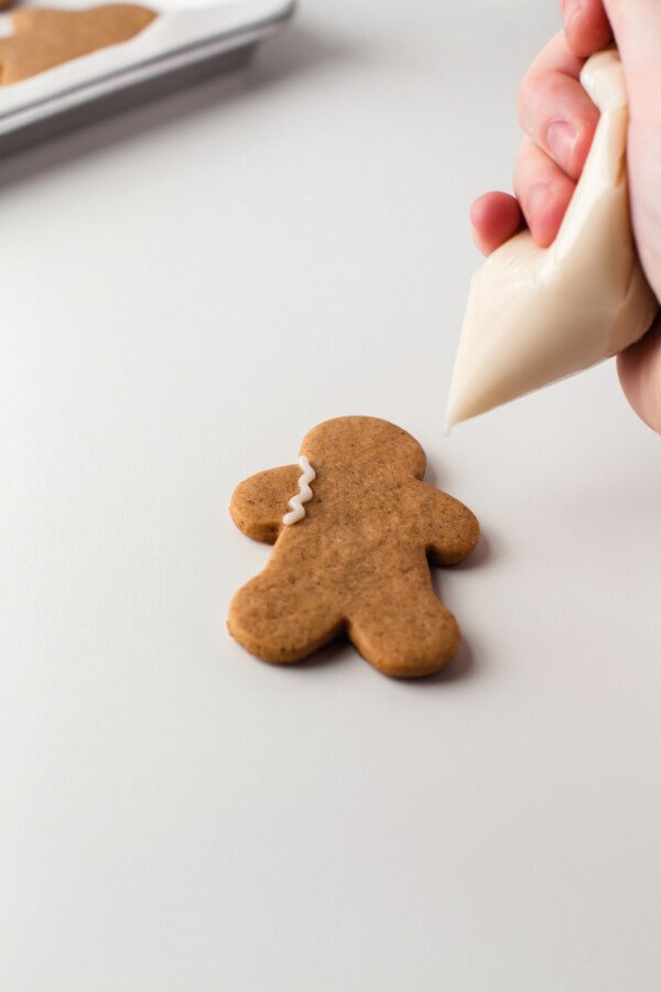 A hand holding a DIY piping bag made out of a zip-top baggie, decorating a gingerbread man cookie.