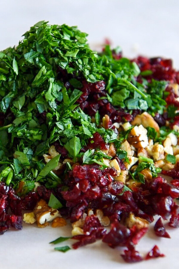 Dried cranberries, pecans and chopped fresh parsley combined in a pile on parchment paper.