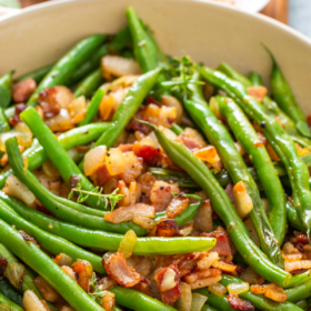 Green beans that are sautéed in bacon fat with onions and crispy bacon bits in a skillet.