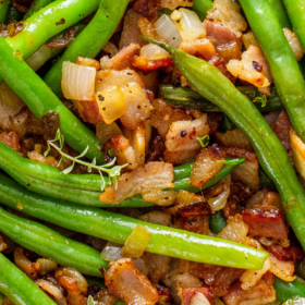 Up close image of green beans that are sautéed in bacon fat with onions and crispy bacon bits in a skillet.