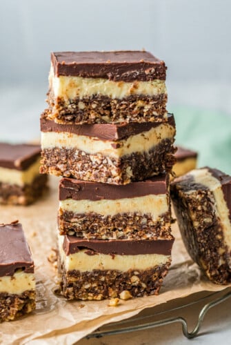 Layered dessert bars stacked on top of each other on a background of parchment and white countertop. Several bars are arranged around the stack.