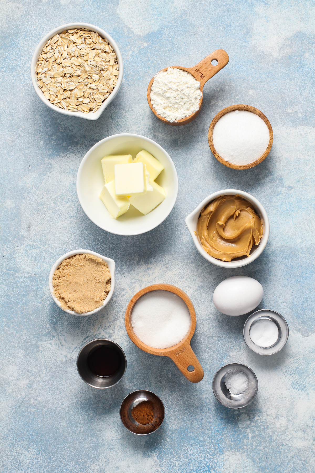 Clockwise from top: rolled oats, flour, white sugar, peanut butter, egg, baking soda, salt, additional white sugar, cinnamon, vanilla, light brown sugar, butter.