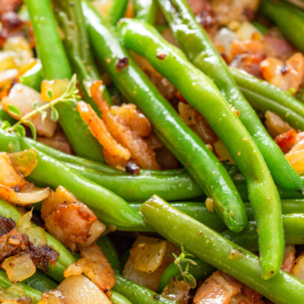 Up close image of green beans that are sautéed in bacon fat with onions and crispy bacon bits in a skillet.