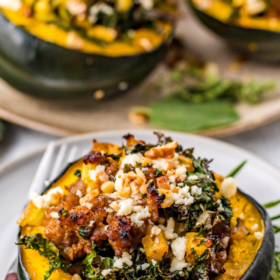 Stuffed acorn squash on a white plate with a fork and with the filling inside the squash.
