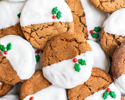 Gingersnap cookies dipped in white chocolate with holly sprinkles stacked on top of each other.