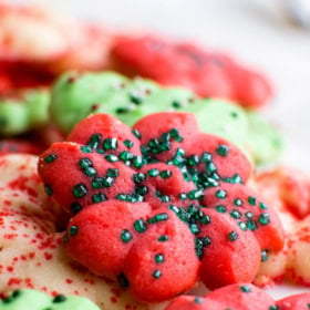 Up close image of a red spritz cookie with green sprinkles on top.