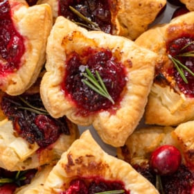 Cranberry Brie Bites stacked on top of each other with fresh rosemary and flakey salt on top.