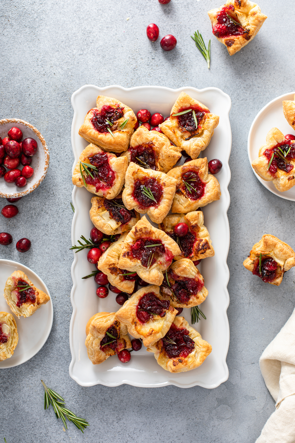 Cranberry Brie Bites on a white plate with cranberries and rosemary scattered around.