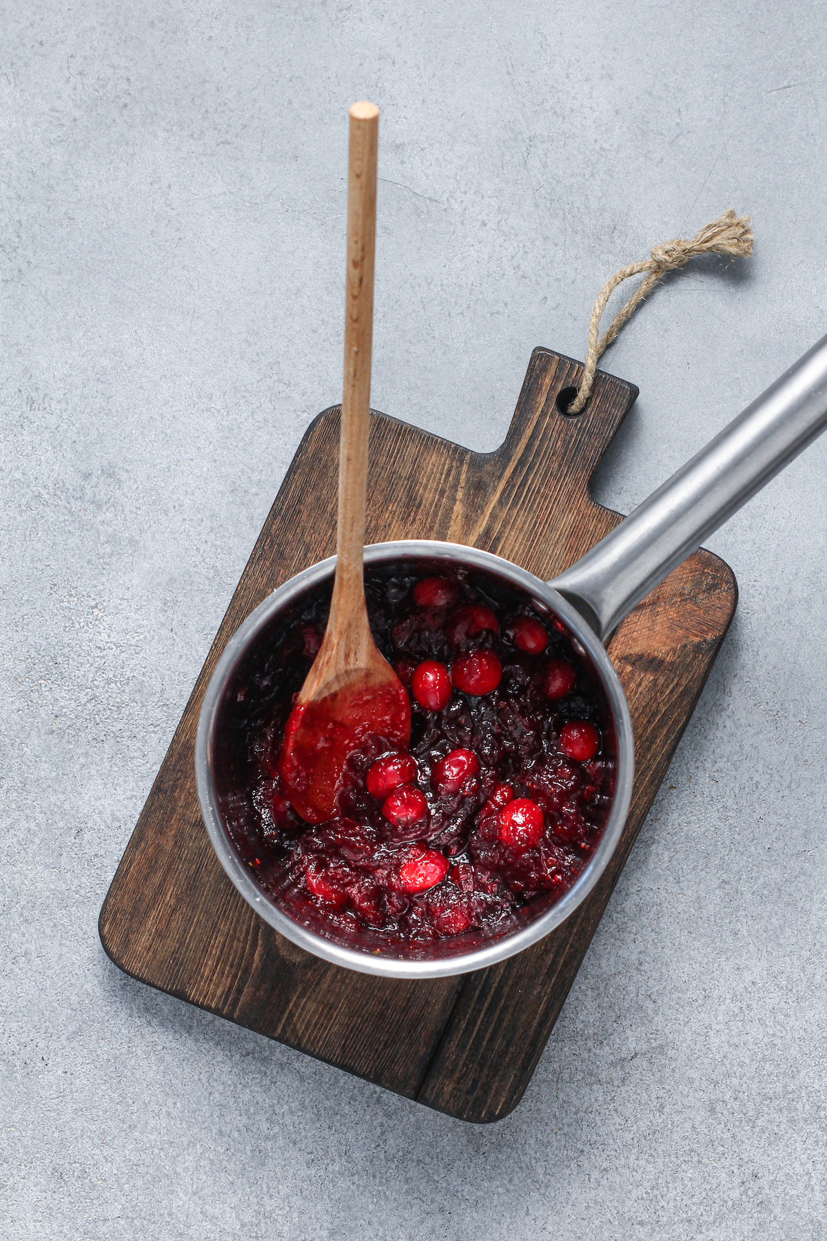Homemade cranberry sauce in a sauce pan with a wooden spoon.