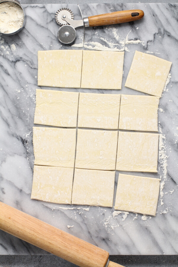 Puff pastry cut into squares on a marble top.