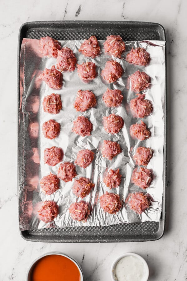 Unbaked chicken meatballs on a foil-lined baking sheet.