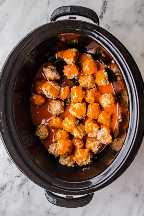 An overhead shot of the insert of a crock pot, with meatballs and sauce inside.