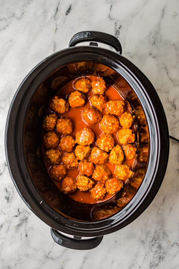 Slow cooked chicken meatballs in buffalo sauce, in the insert of a crockpot.