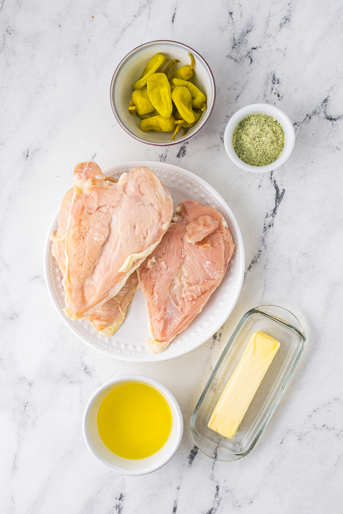 Clockwise from top: Pepperoncini, dry ranch seasoning, butter, pepperoncini brine, and boneless skinless, chicken breasts.