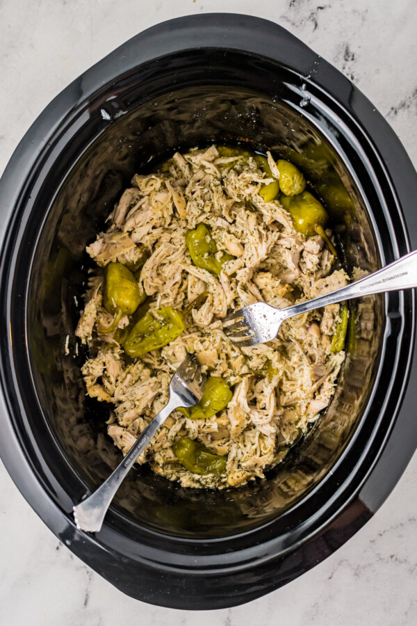 Overhead shot of a crockpot insert with shredded chicken and peppers. Two forks are resting in the chicken.