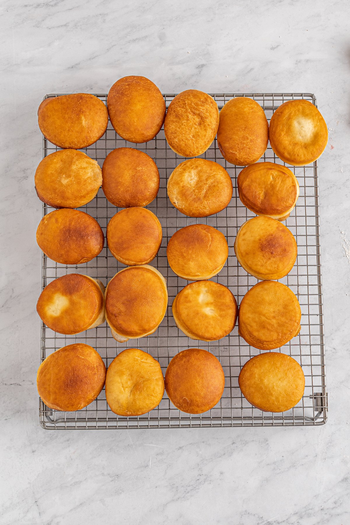 Fried, unfilled donuts on a cooling rack.