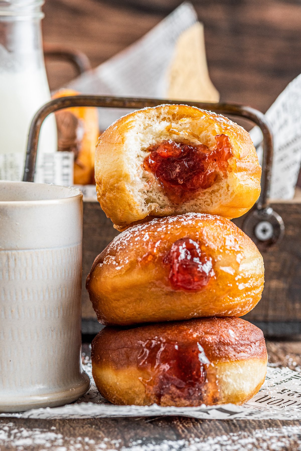 A stack of three jelly-filled donuts. A bite has been taken out of the top donut.