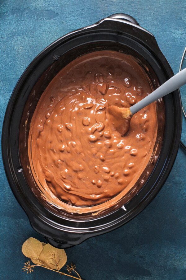 Melted chocolate and peanuts in a crockpot with a spatula stirring it.