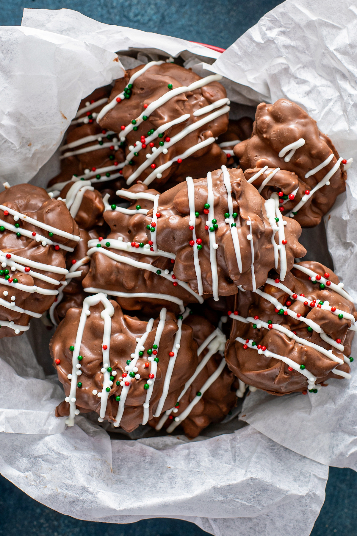 Overhead image of crockpot candy clusters in a Christmas Cookie tin with tissue paper.