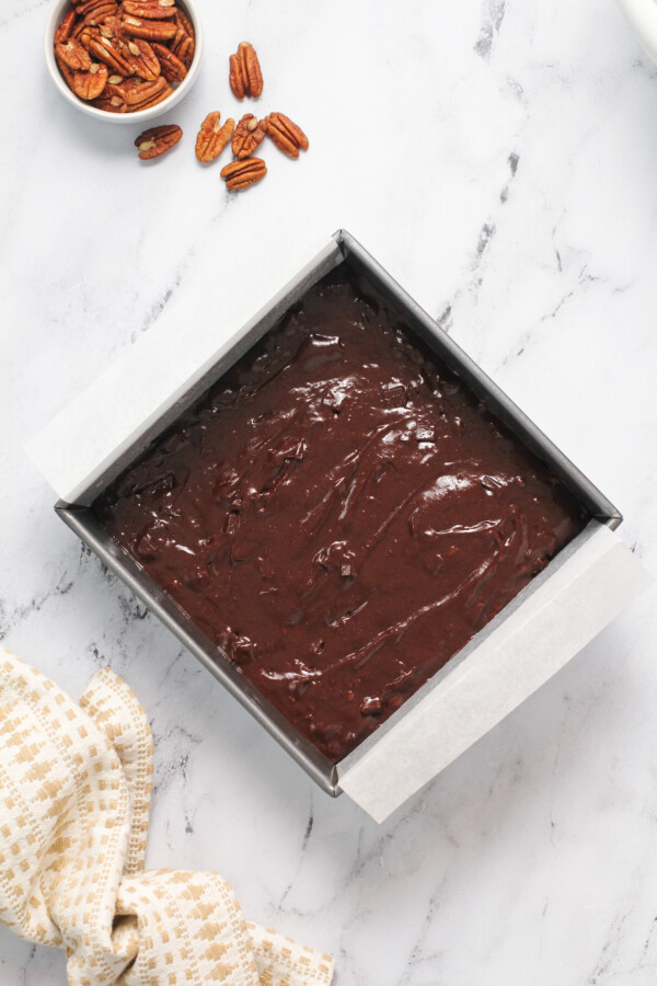 Raw brownie dough in a square baking dish with parchment paper.