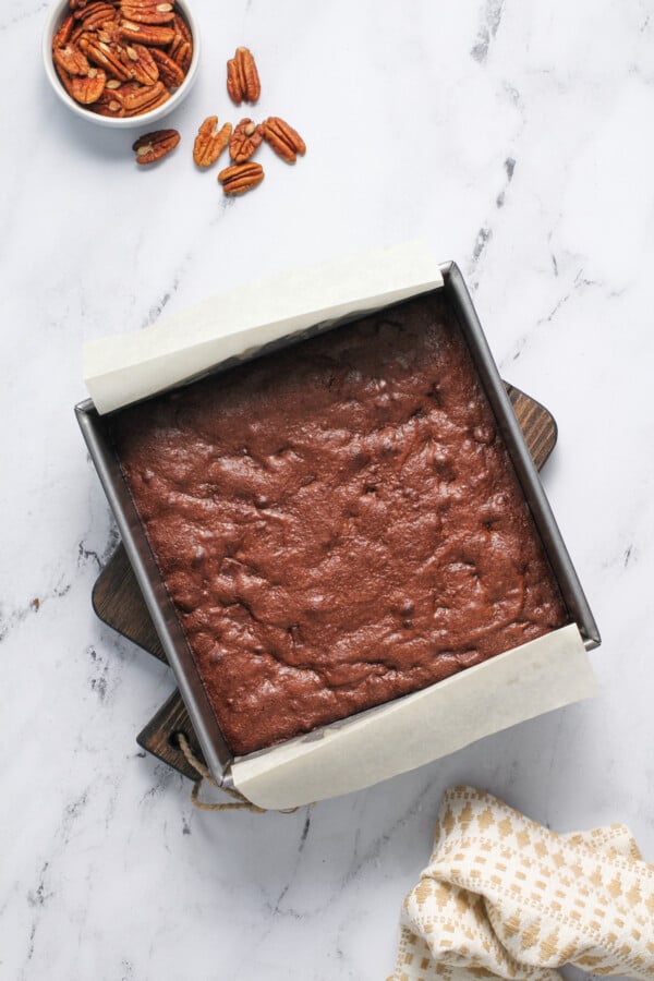 Brownies in a baking dish with parchment paper on cutting board.