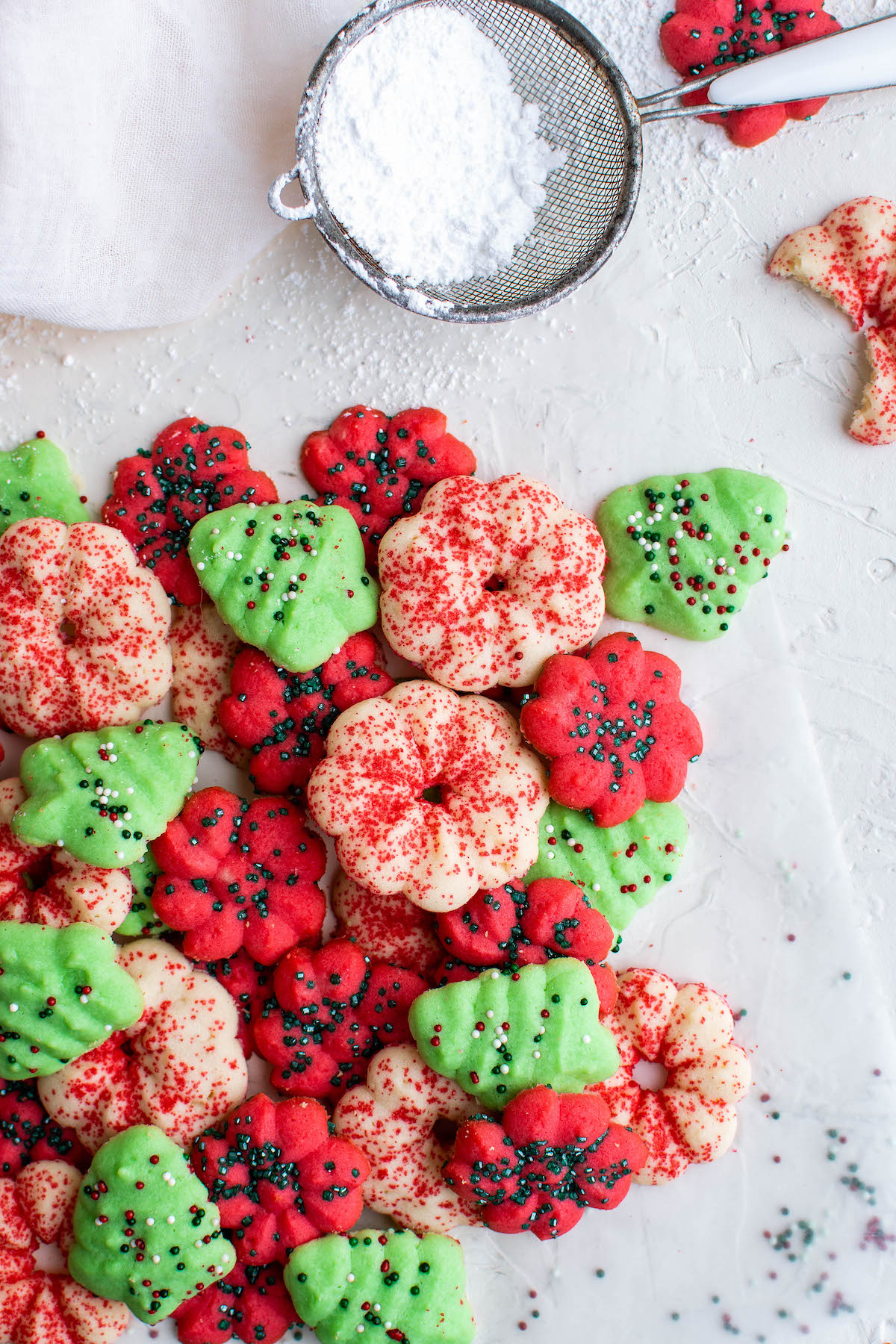 Christmas spritz cookies on parchment paper with a sifter filled with powdered sugar.