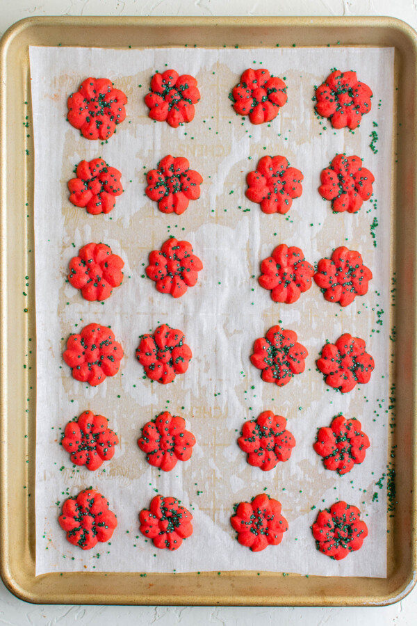 Red spritz cookies with green sprinkles on a cookie sheet.